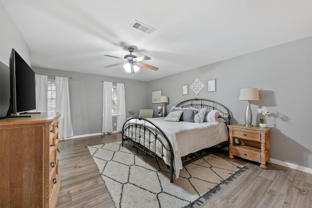 bedroom with light wood-style floors, visible vents, ceiling fan, and baseboards