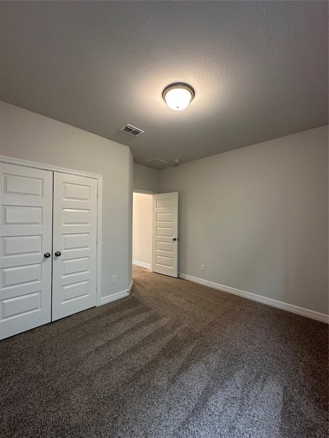 unfurnished bedroom with dark colored carpet, a textured ceiling, and a closet