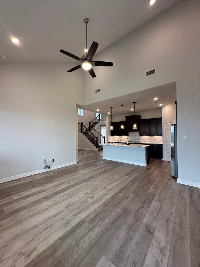 unfurnished living room with hardwood / wood-style floors, high vaulted ceiling, and ceiling fan