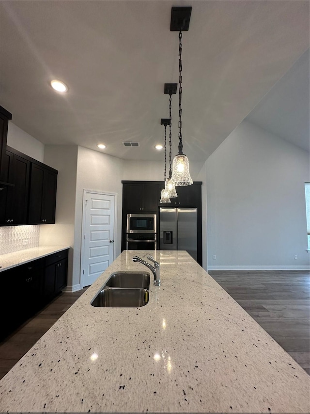 kitchen featuring pendant lighting, sink, stainless steel appliances, light stone counters, and an island with sink