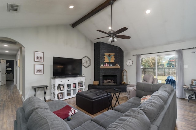 living room featuring vaulted ceiling with beams, dark wood-type flooring, a large fireplace, and ceiling fan