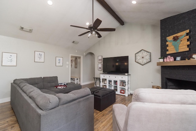 living room featuring high vaulted ceiling, beamed ceiling, hardwood / wood-style flooring, ceiling fan, and a brick fireplace