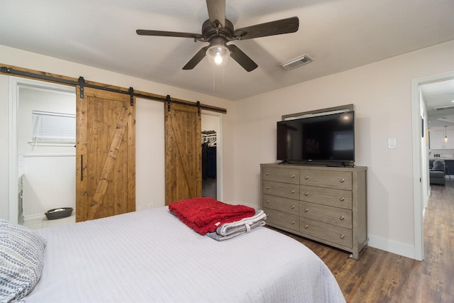 bedroom with dark wood-type flooring, ceiling fan, a barn door, a spacious closet, and a closet