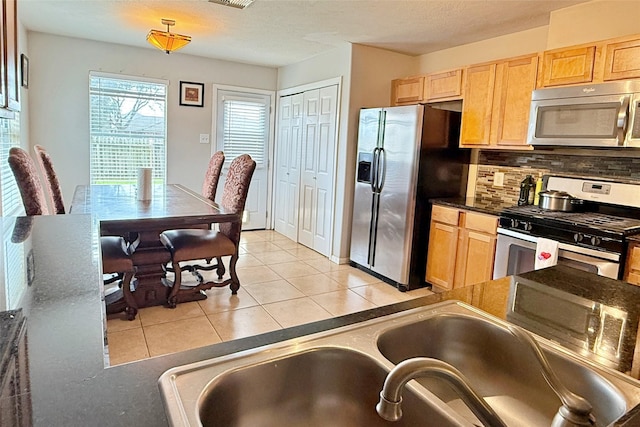 kitchen featuring sink, a textured ceiling, light tile patterned floors, appliances with stainless steel finishes, and decorative backsplash