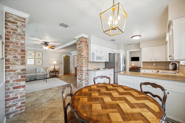 dining area featuring sink, ornate columns, crown molding, a textured ceiling, and ceiling fan with notable chandelier