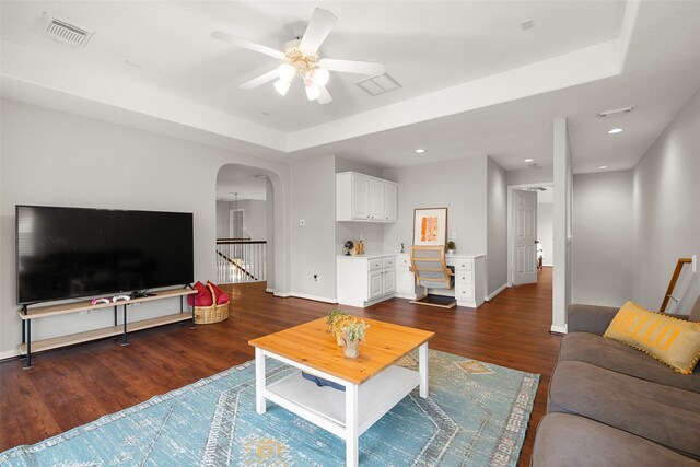 living room featuring a tray ceiling, built in desk, dark hardwood / wood-style floors, and ceiling fan