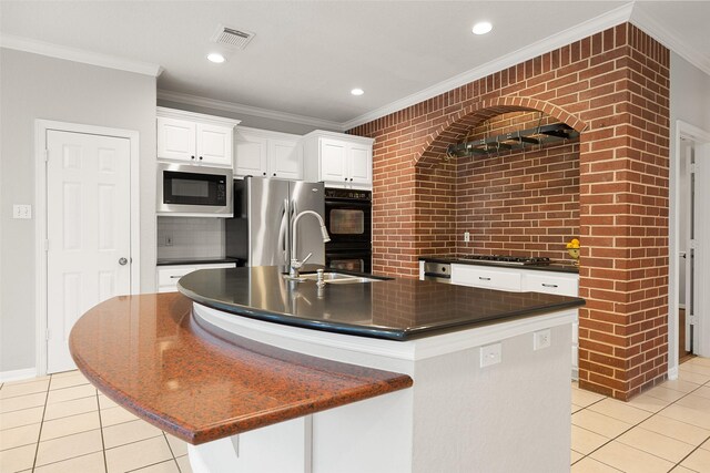 kitchen featuring brick wall, sink, white cabinets, light tile patterned floors, and a center island with sink