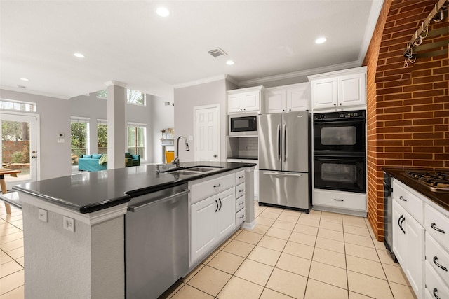 kitchen with an island with sink, sink, white cabinets, light tile patterned floors, and stainless steel appliances