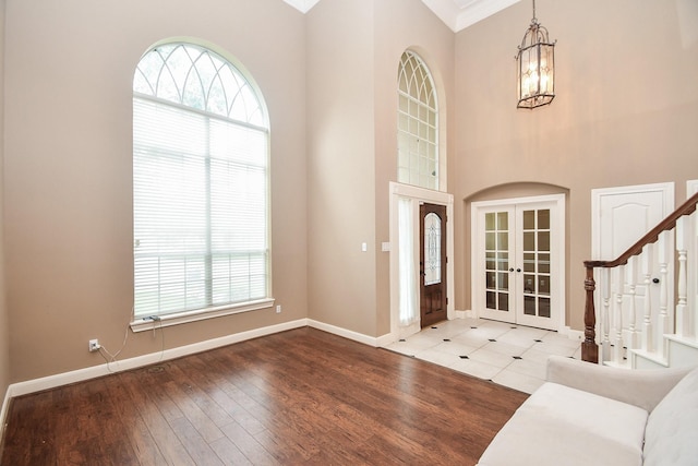 entryway with hardwood / wood-style flooring, a towering ceiling, an inviting chandelier, and french doors