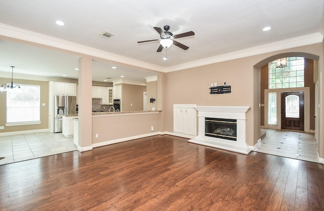 unfurnished living room with ornamental molding, ceiling fan with notable chandelier, and light wood-type flooring