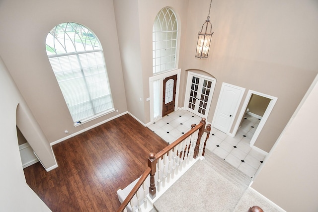 entrance foyer with an inviting chandelier, a towering ceiling, french doors, and hardwood / wood-style flooring