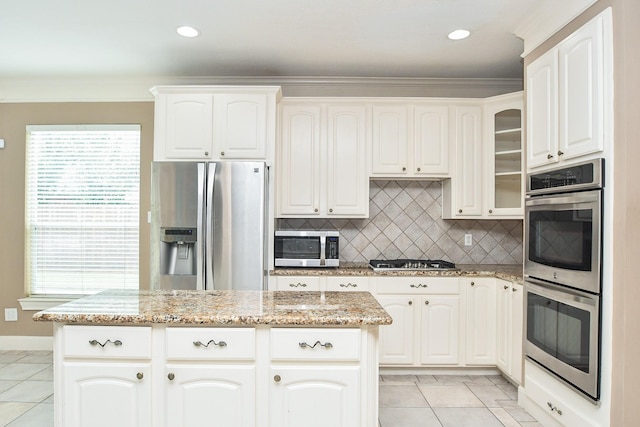 kitchen featuring light tile patterned floors, stainless steel appliances, light stone counters, white cabinets, and a kitchen island