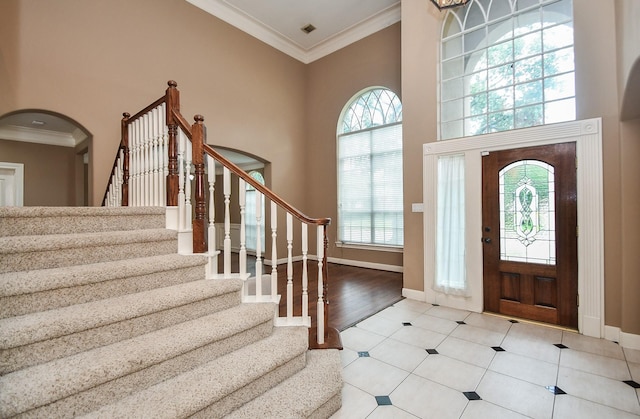 foyer entrance featuring crown molding, a towering ceiling, and light tile patterned floors