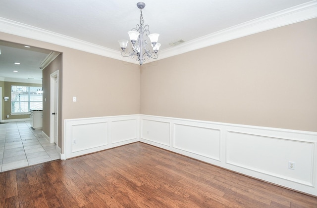 empty room featuring wood-type flooring, ornamental molding, and a notable chandelier