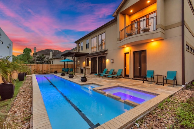 pool at dusk with a patio and an in ground hot tub