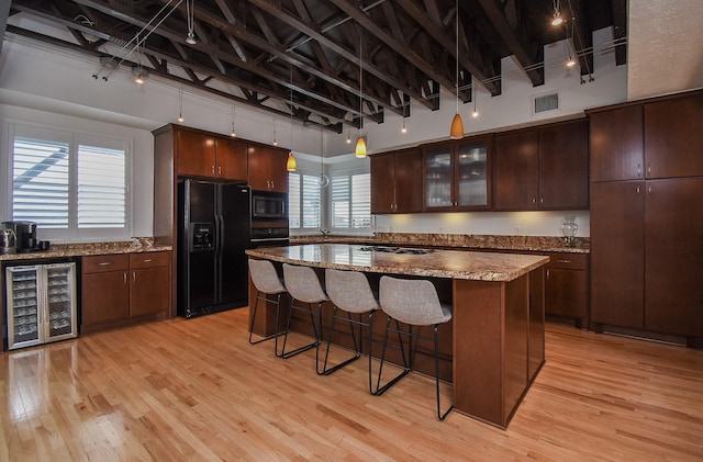 kitchen with beverage cooler, built in microwave, a kitchen island, black fridge, and dark brown cabinetry