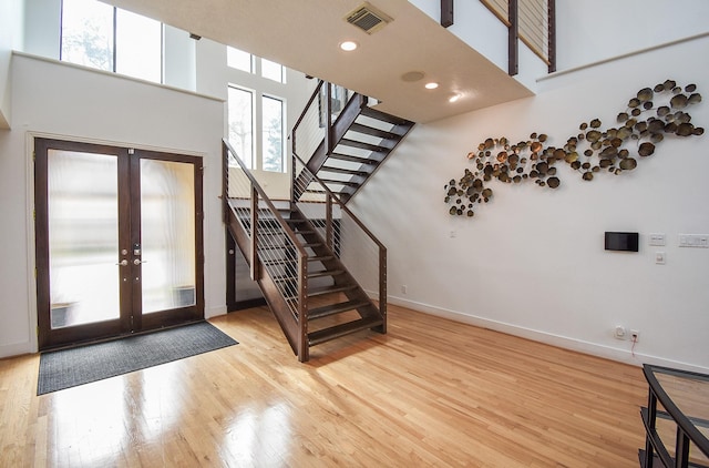 foyer featuring french doors, a towering ceiling, and light hardwood / wood-style flooring