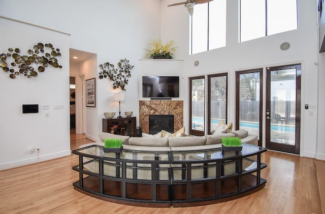 living room with ceiling fan, light hardwood / wood-style flooring, a premium fireplace, and a towering ceiling