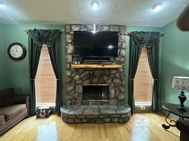 living area with a textured ceiling, a stone fireplace, wood finished floors, and baseboards