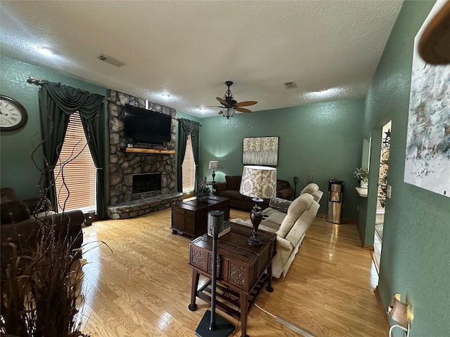 living area with a fireplace, wood finished floors, visible vents, and a ceiling fan