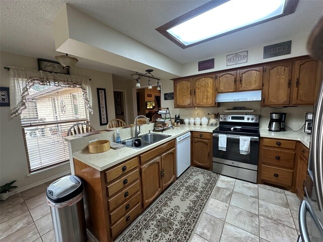 kitchen with dishwasher, a peninsula, under cabinet range hood, stainless steel range with electric stovetop, and a sink