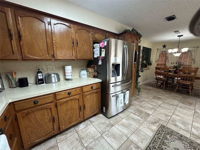 kitchen with a textured ceiling, light countertops, brown cabinetry, stainless steel fridge, and decorative light fixtures