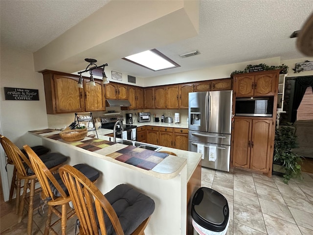 kitchen with visible vents, appliances with stainless steel finishes, a peninsula, light countertops, and under cabinet range hood