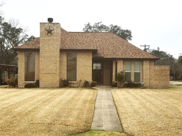 view of front facade featuring roof with shingles, brick siding, a chimney, and a front yard