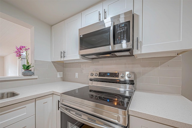 kitchen featuring tasteful backsplash, white cabinetry, sink, light stone counters, and stainless steel appliances