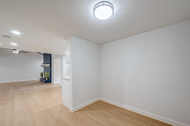 spare room featuring ceiling fan, a fireplace, light hardwood / wood-style flooring, and a textured ceiling