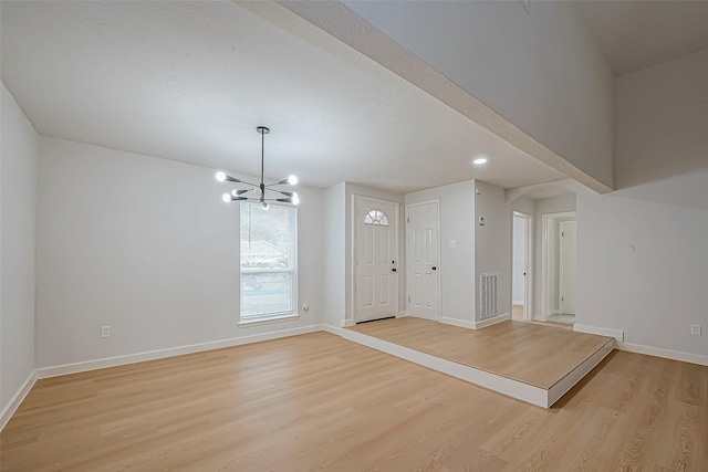 spare room with a notable chandelier and light wood-type flooring