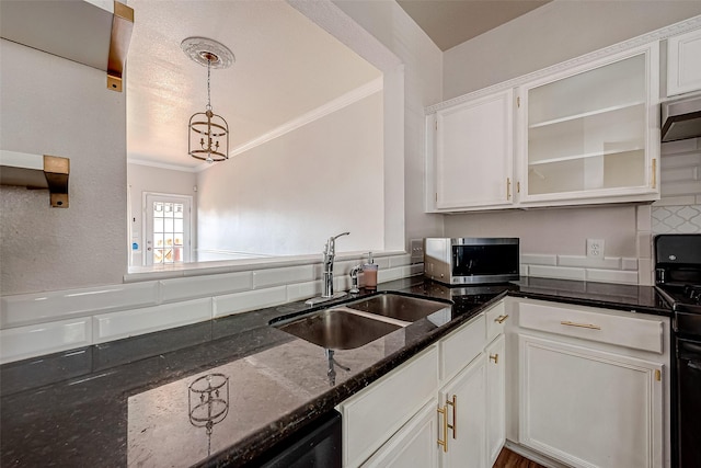 kitchen with sink, ornamental molding, white cabinets, decorative light fixtures, and dark stone counters