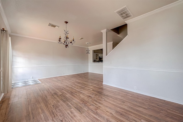 empty room with crown molding, an inviting chandelier, and hardwood / wood-style floors