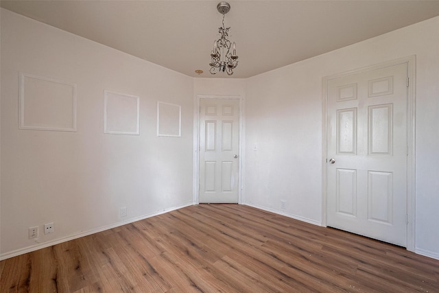 empty room with wood-type flooring and a chandelier