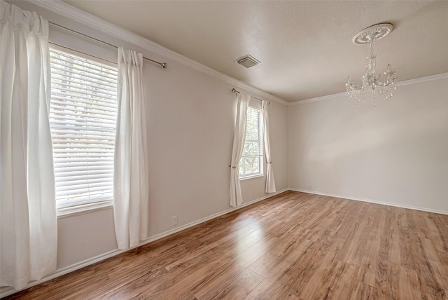 spare room with crown molding, a chandelier, hardwood / wood-style floors, and a wealth of natural light