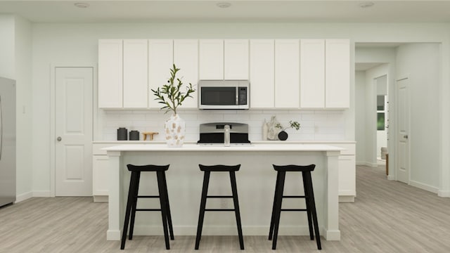 kitchen with stove, a kitchen island with sink, white cabinets, and decorative backsplash