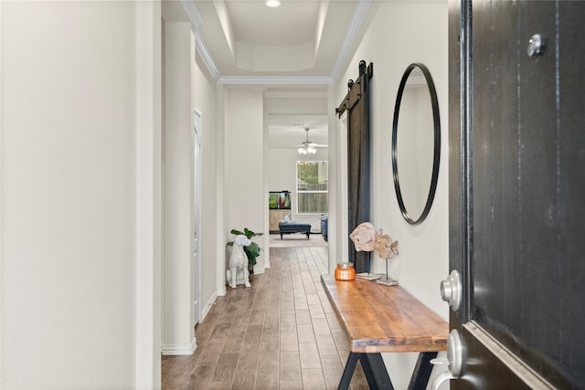 hall with crown molding, wood-type flooring, a barn door, and a raised ceiling