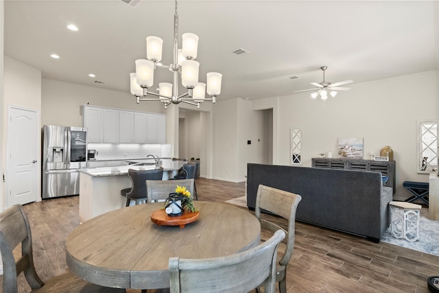 dining space with ceiling fan with notable chandelier, dark wood-type flooring, and sink