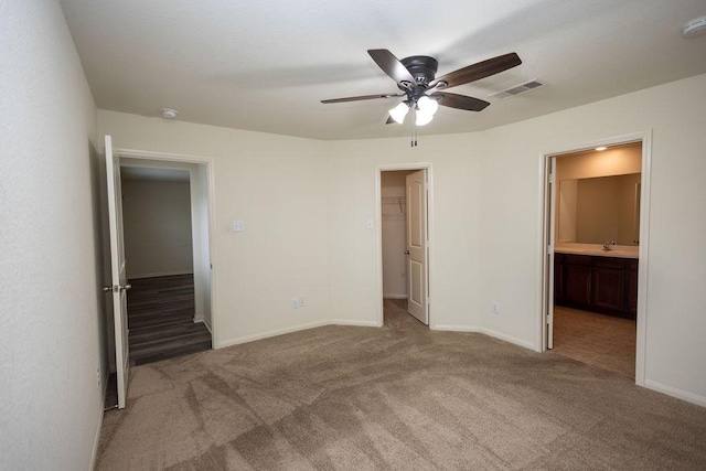 unfurnished bedroom featuring connected bathroom, carpet floors, sink, a walk in closet, and ceiling fan