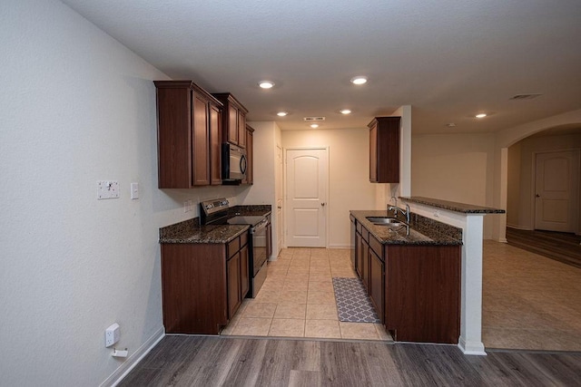 kitchen featuring sink, kitchen peninsula, stainless steel range with electric cooktop, and dark stone counters