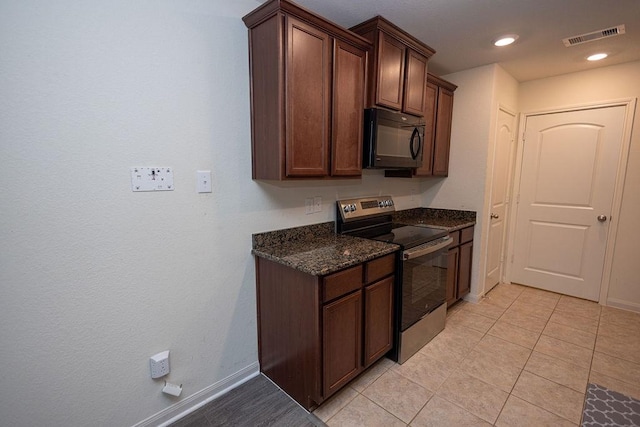 kitchen featuring stainless steel electric stove, dark brown cabinets, light tile patterned flooring, and dark stone counters