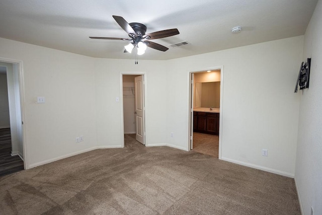 unfurnished bedroom featuring ceiling fan, ensuite bathroom, carpet, a spacious closet, and a closet