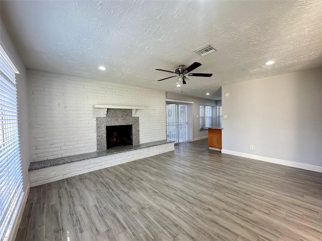 unfurnished living room featuring ceiling fan, a fireplace, hardwood / wood-style floors, and a textured ceiling