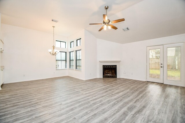 unfurnished living room with a healthy amount of sunlight, ceiling fan with notable chandelier, light hardwood / wood-style floors, and french doors