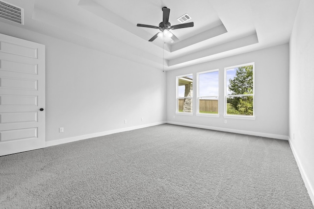 carpeted empty room with baseboards, a tray ceiling, visible vents, and ceiling fan