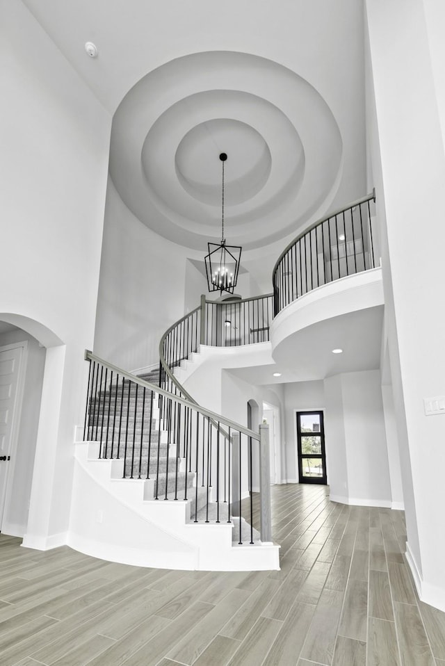 stairway featuring a chandelier, baseboards, a towering ceiling, wood finished floors, and arched walkways