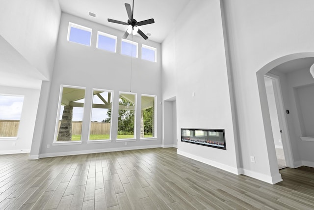 unfurnished living room with a ceiling fan, visible vents, plenty of natural light, and wood finished floors