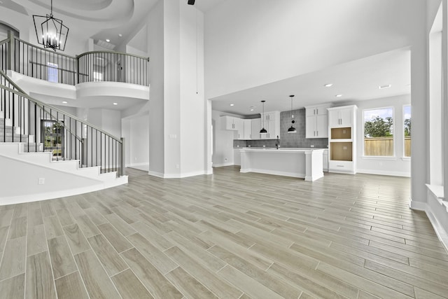 unfurnished living room with baseboards, stairs, wood finish floors, and a notable chandelier
