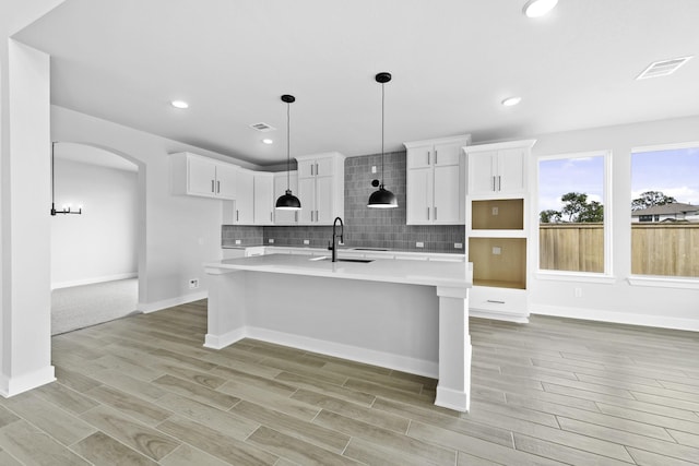 kitchen featuring an island with sink, a sink, wood finish floors, arched walkways, and decorative backsplash