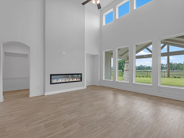 32602 Fly Fish Way, Fulshear, TX 77441 - unfurnished living room with a towering ceiling, a ceiling fan, a glass covered fireplace, arched walkways, and light wood-style flooring